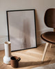 Framed artwork on a wall with a vase, mug, and chair in a room.