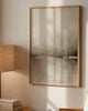Nestled corner of a room with a lamp, books, and a chair against a wall with a framed abstract painting.