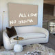Modern living room with a white sofa, decorative pillows, and a wall art piece with text that reads "all love no drama" in white text over a soft neutral beige background