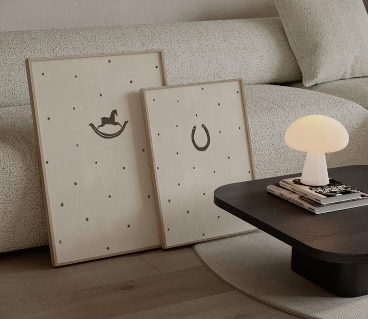 Two framed pictures with rocking horse and horseshoe designs on a textured wall, next to a lamp on a table.