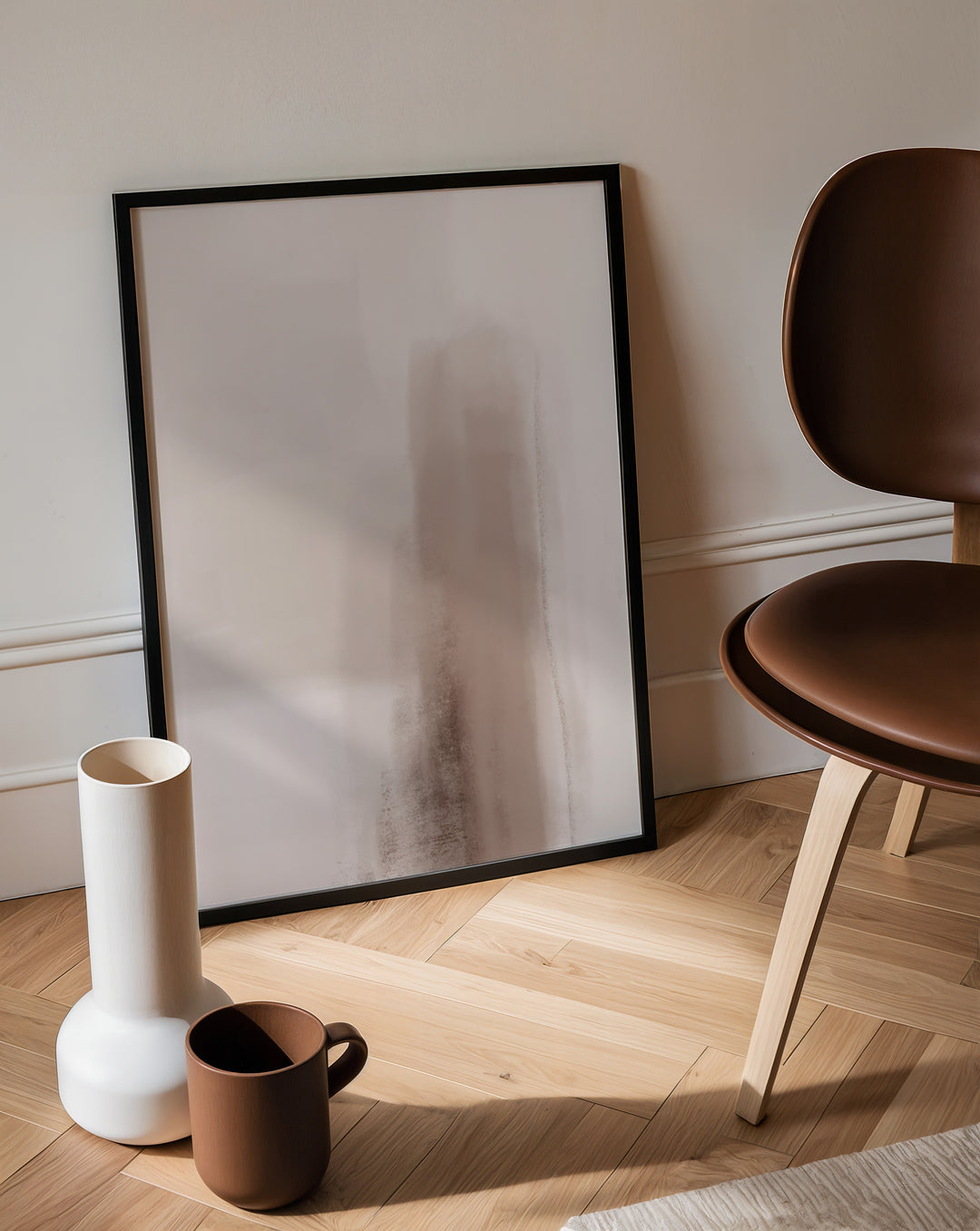 Framed artwork on a wall with a vase, mug, and chair in a room.