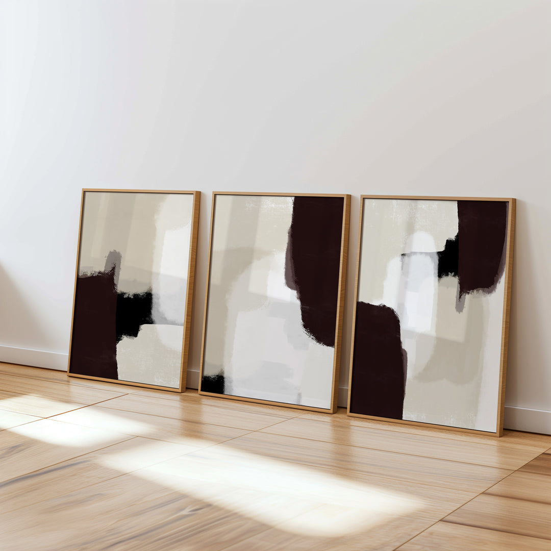 Three abstract art pieces in oak style frames on a white wall.