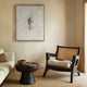 Modern living room with a black armchair, white sofa, and abstract art on the wall. The artwork is a large abstract canvas with grey tones and a dark silhouette etched figure in the centre.