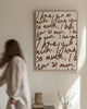 Woman in a white robe standing by a bed in a bedroom with a wall art print on a beige background with text that reads "i love you so much"