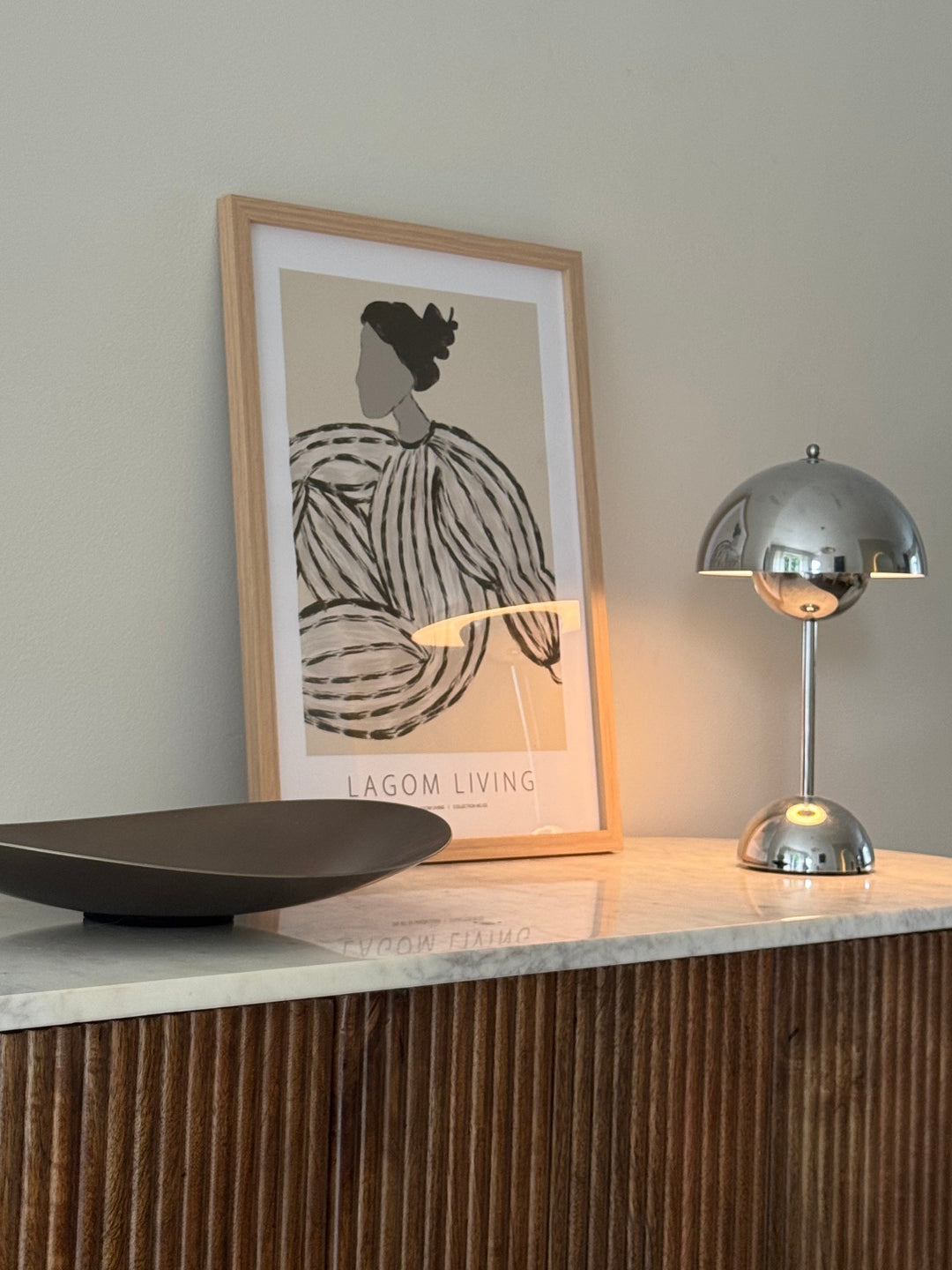 Wall-mounted lamp with a framed picture on a wall next to a wooden shelf.