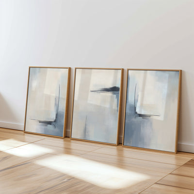Three abstract wall prints in blue, cream and beige neutral tones with oak wood style frames in a modern living space with light hardwood floors